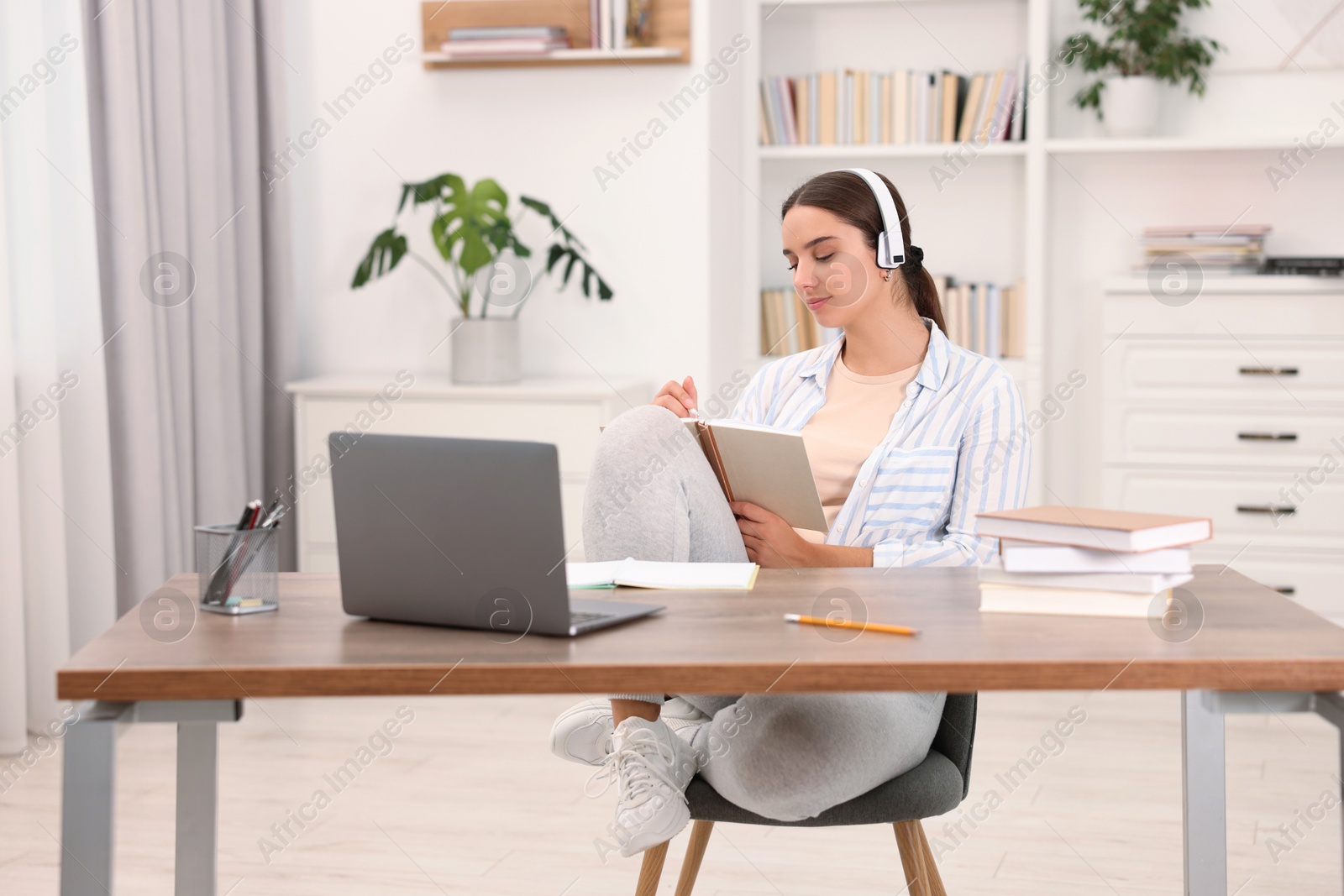 Photo of Student in headphones studying at wooden table indoors