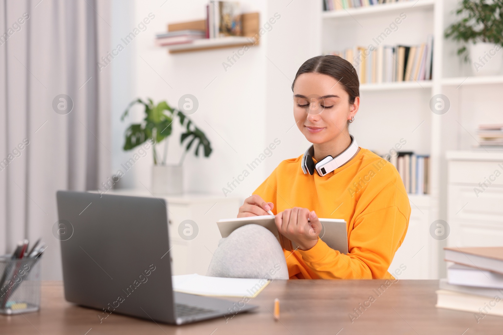 Photo of Student with headphones taking notes while studying indoors