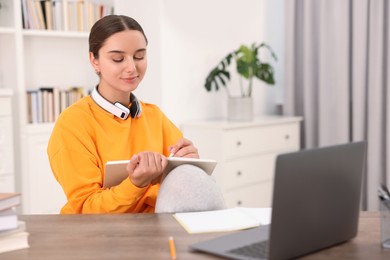 Student with headphones taking notes while studying indoors