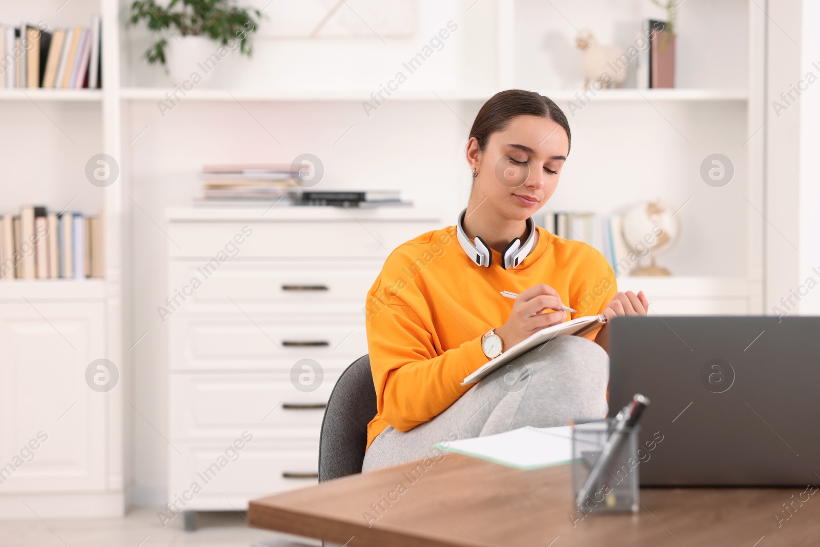 Photo of Student with headphones taking notes while studying indoors