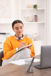 Photo of Student with headphones taking notes while studying indoors