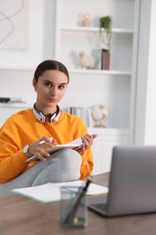 Photo of Student with headphones and notebook studying indoors