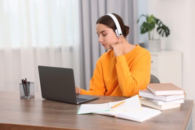 Student in headphones studying with laptop at wooden table indoors