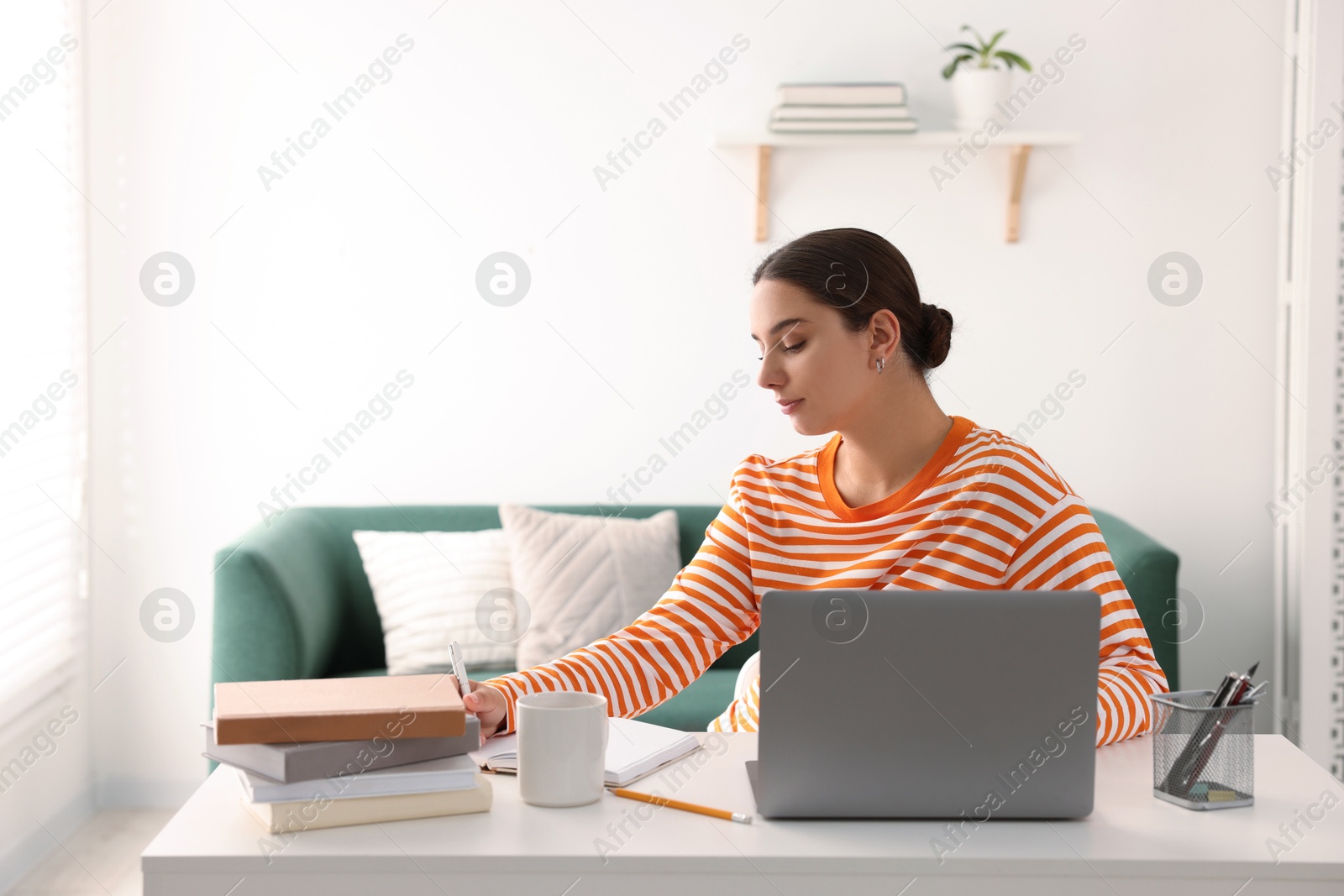 Photo of Student taking notes while studying at table indoors