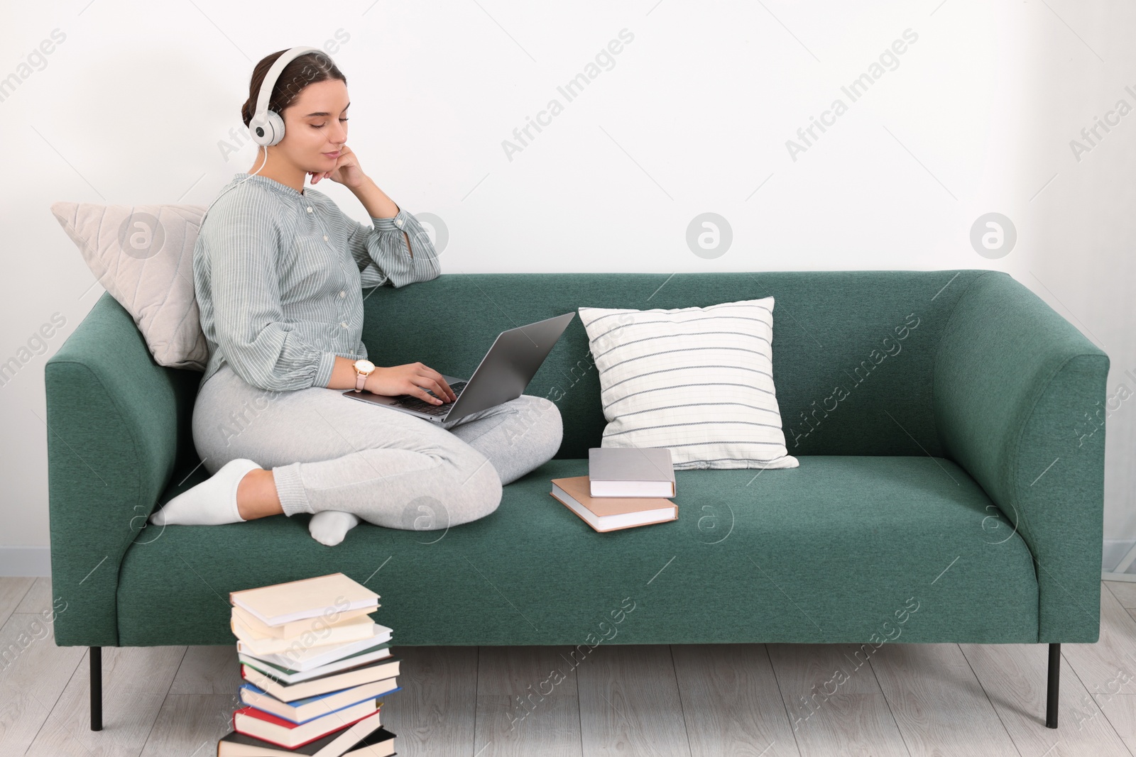 Photo of Student in headphones studying with laptop on sofa at home