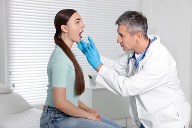 Photo of Doctor examining woman's throat with tongue depressor in clinic