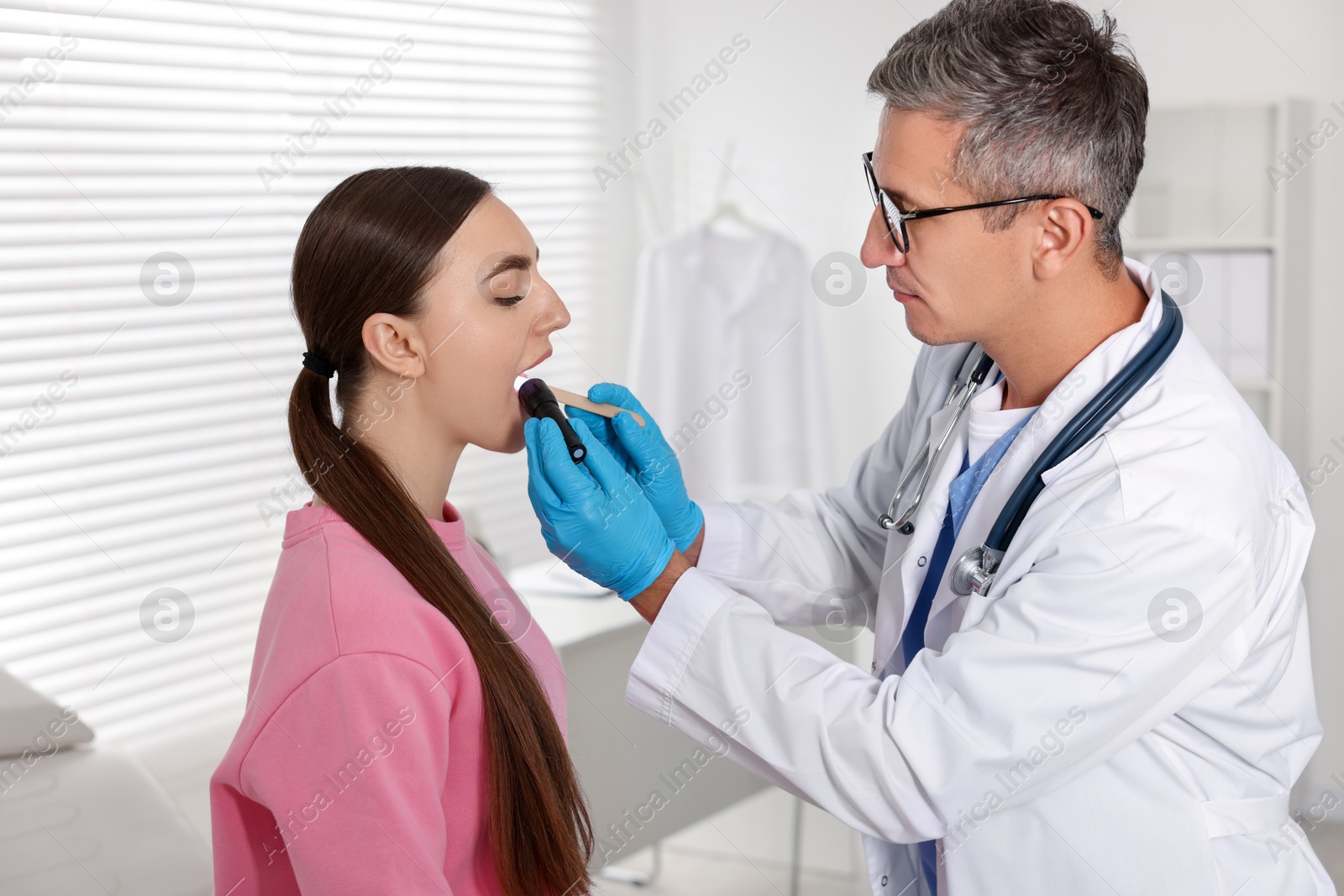 Photo of Doctor examining woman's throat with flashlight tongue depressor in clinic