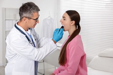 Photo of Doctor examining woman's throat with flashlight tongue depressor in clinic