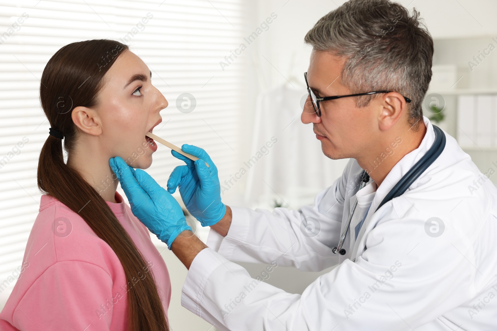 Photo of Doctor examining woman's throat with tongue depressor in clinic