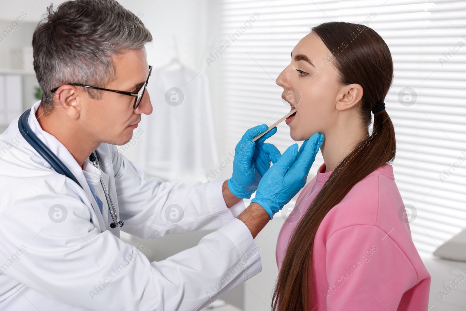 Photo of Doctor examining woman's throat with tongue depressor in clinic