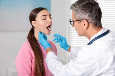 Photo of Doctor examining woman's throat with tongue depressor in clinic