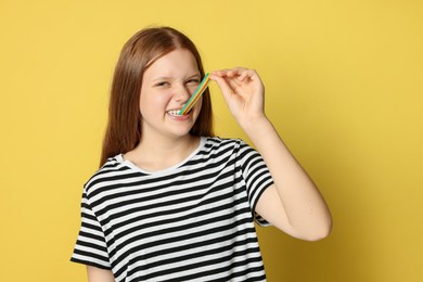 Photo of Teenage girl eating tasty rainbow sour belt on yellow background