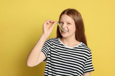 Photo of Teenage girl eating tasty rainbow sour belt on yellow background