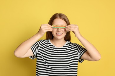 Happy teenage girl with tasty rainbow sour belt closing her eyes on yellow background