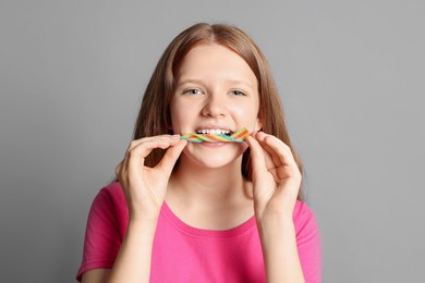 Photo of Teenage girl eating tasty rainbow sour belt on grey background