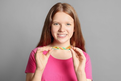 Photo of Happy teenage girl with tasty rainbow sour belt on grey background