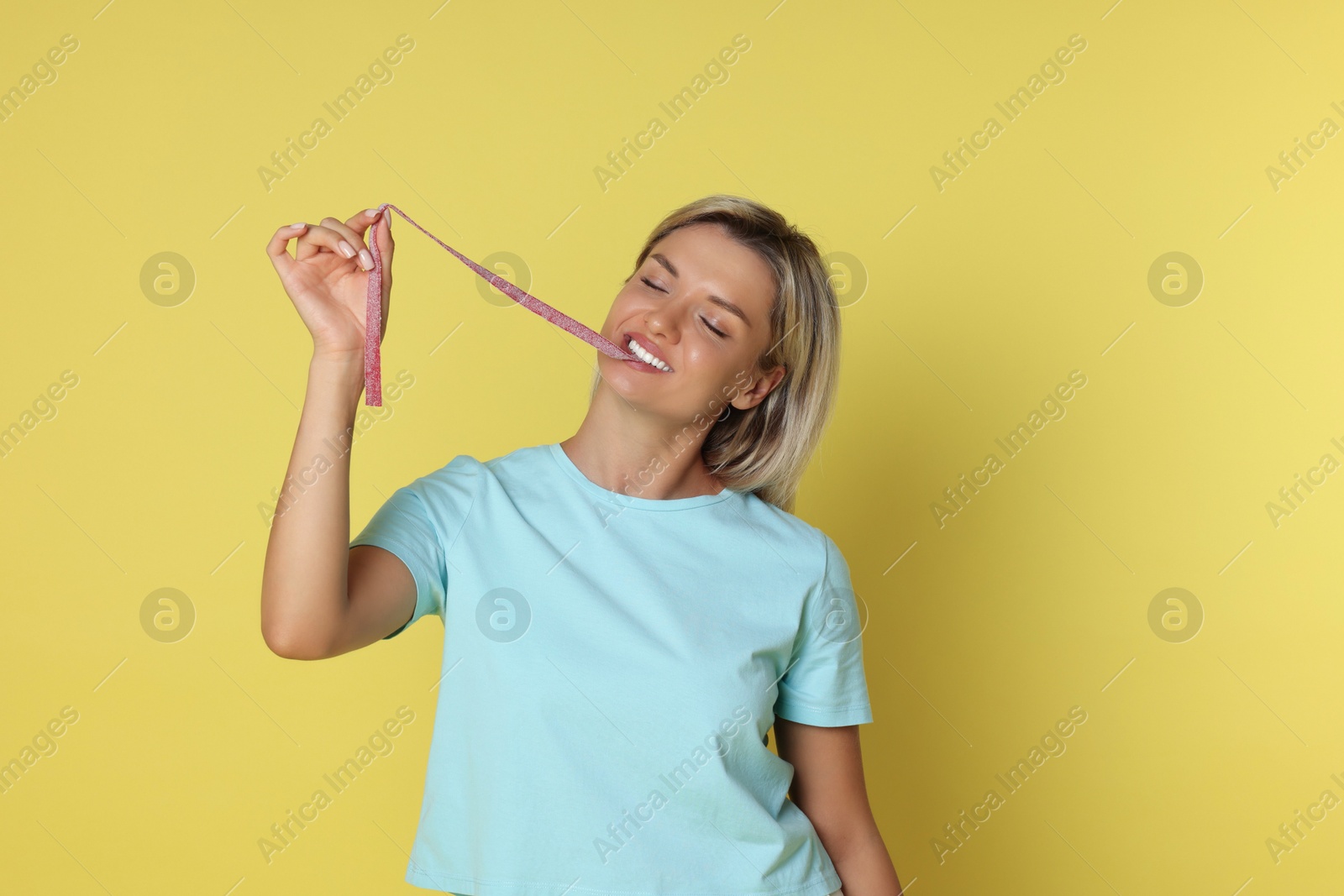 Photo of Young woman eating tasty gummy candy on yellow background