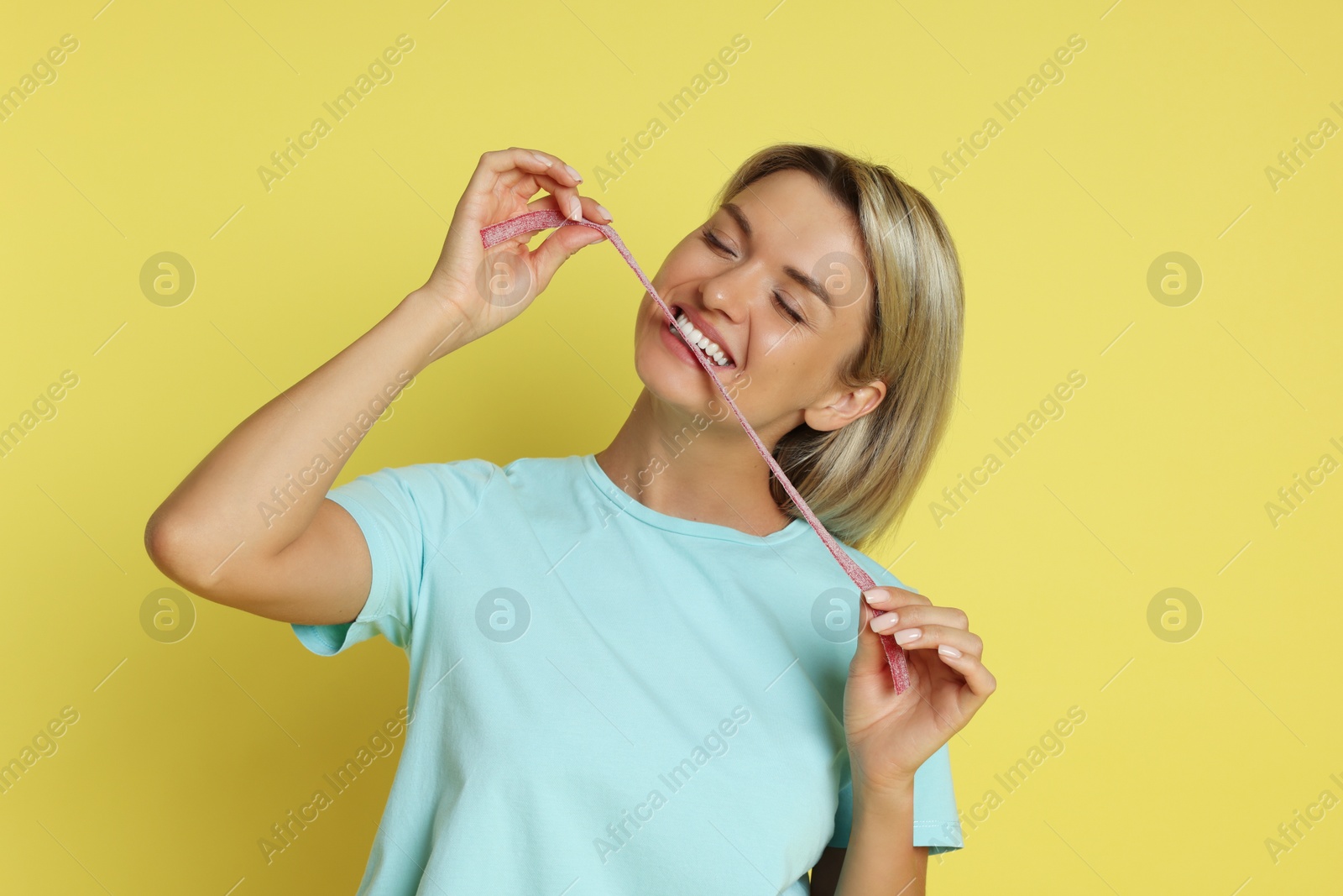 Photo of Young woman eating tasty gummy candy on yellow background