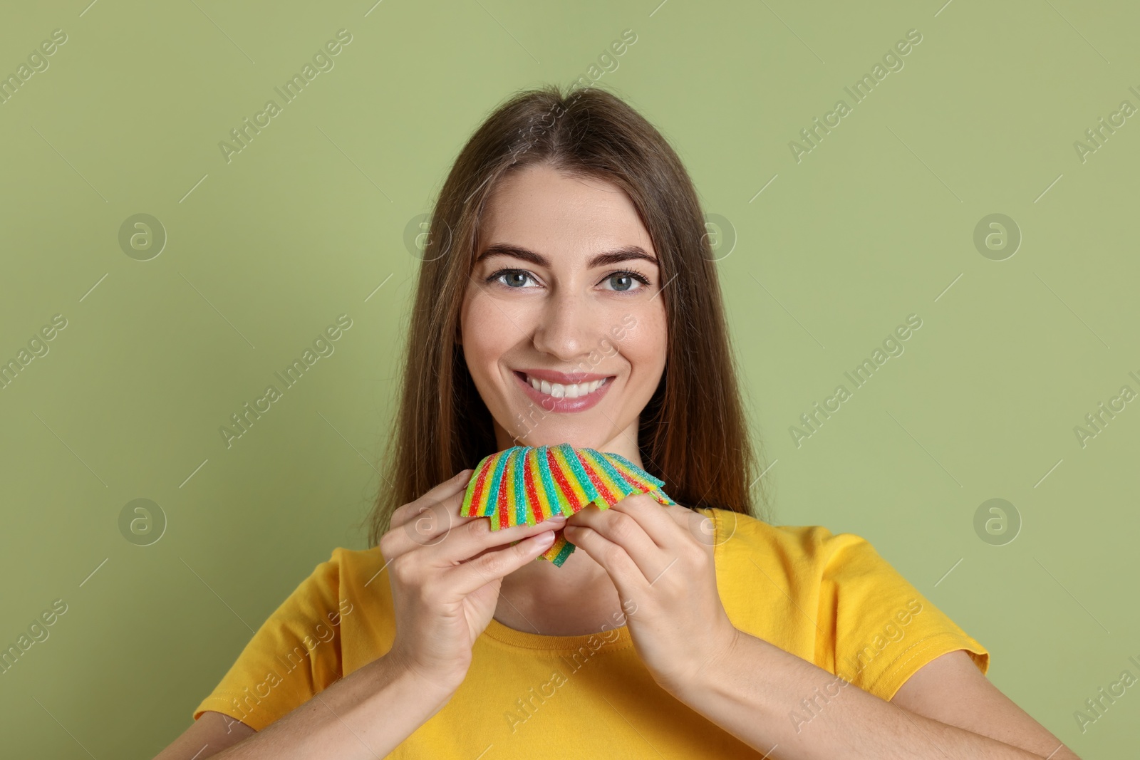 Photo of Happy young woman with tasty rainbow sour belts on olive background