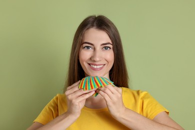 Happy young woman with tasty rainbow sour belts on olive background