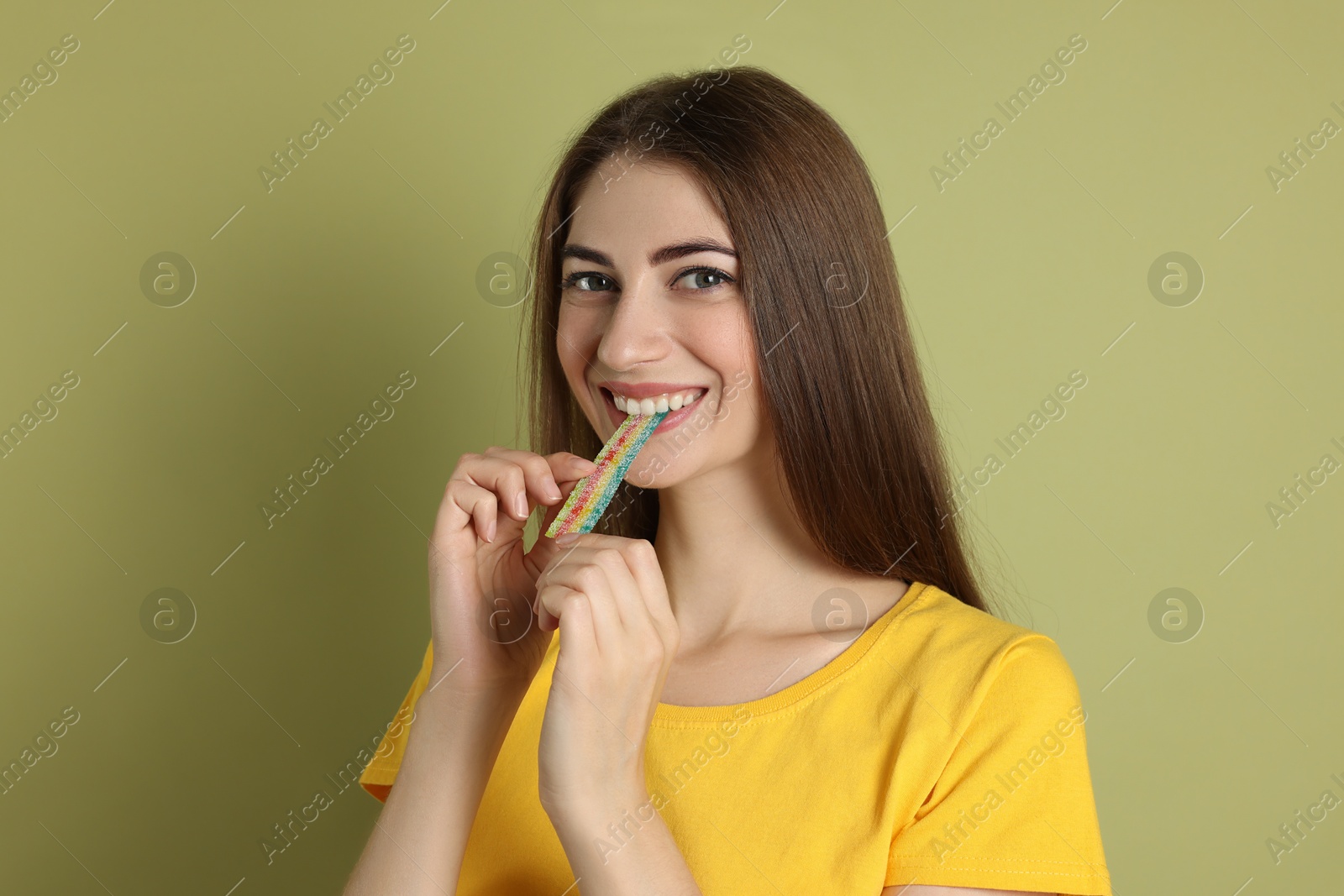 Photo of Young woman eating tasty rainbow sour belt on olive background