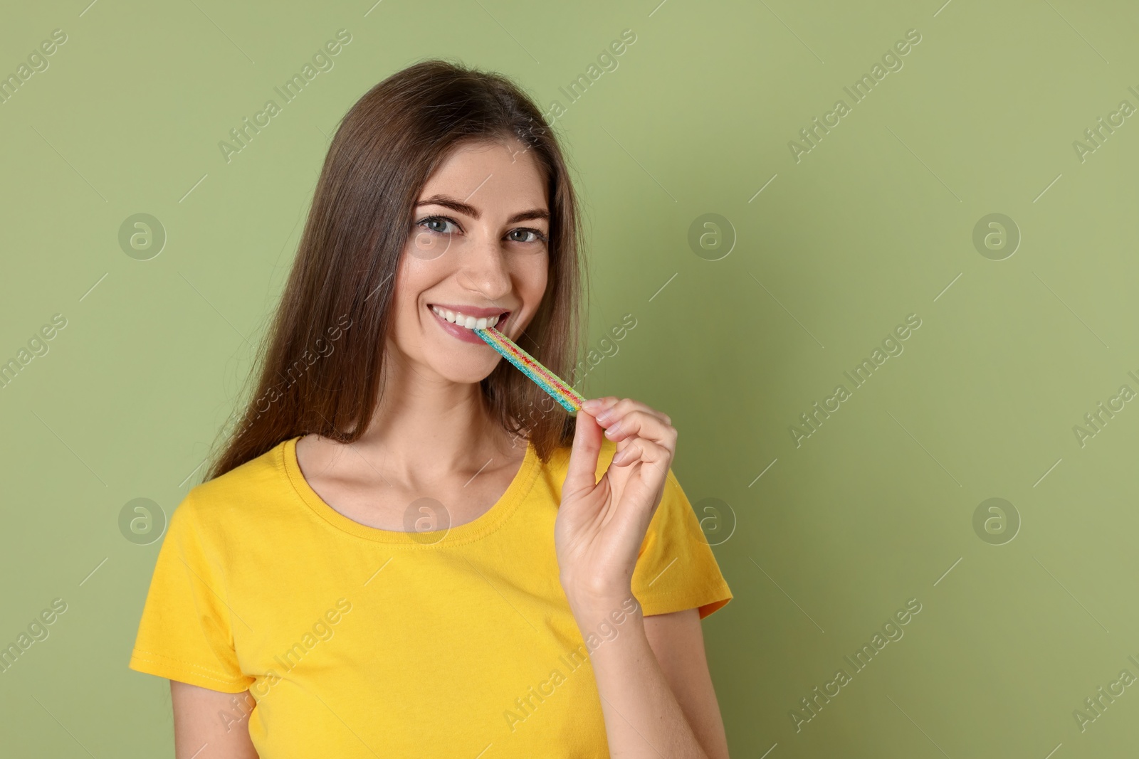 Photo of Young woman eating tasty rainbow sour belt on olive background, space for text