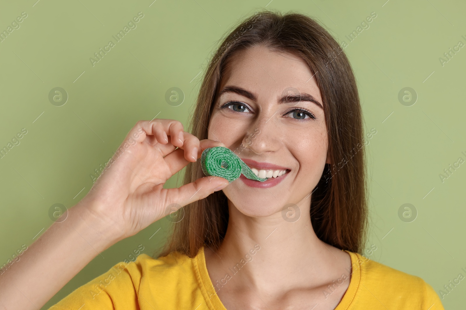 Photo of Young woman eating tasty gummy candy on olive background