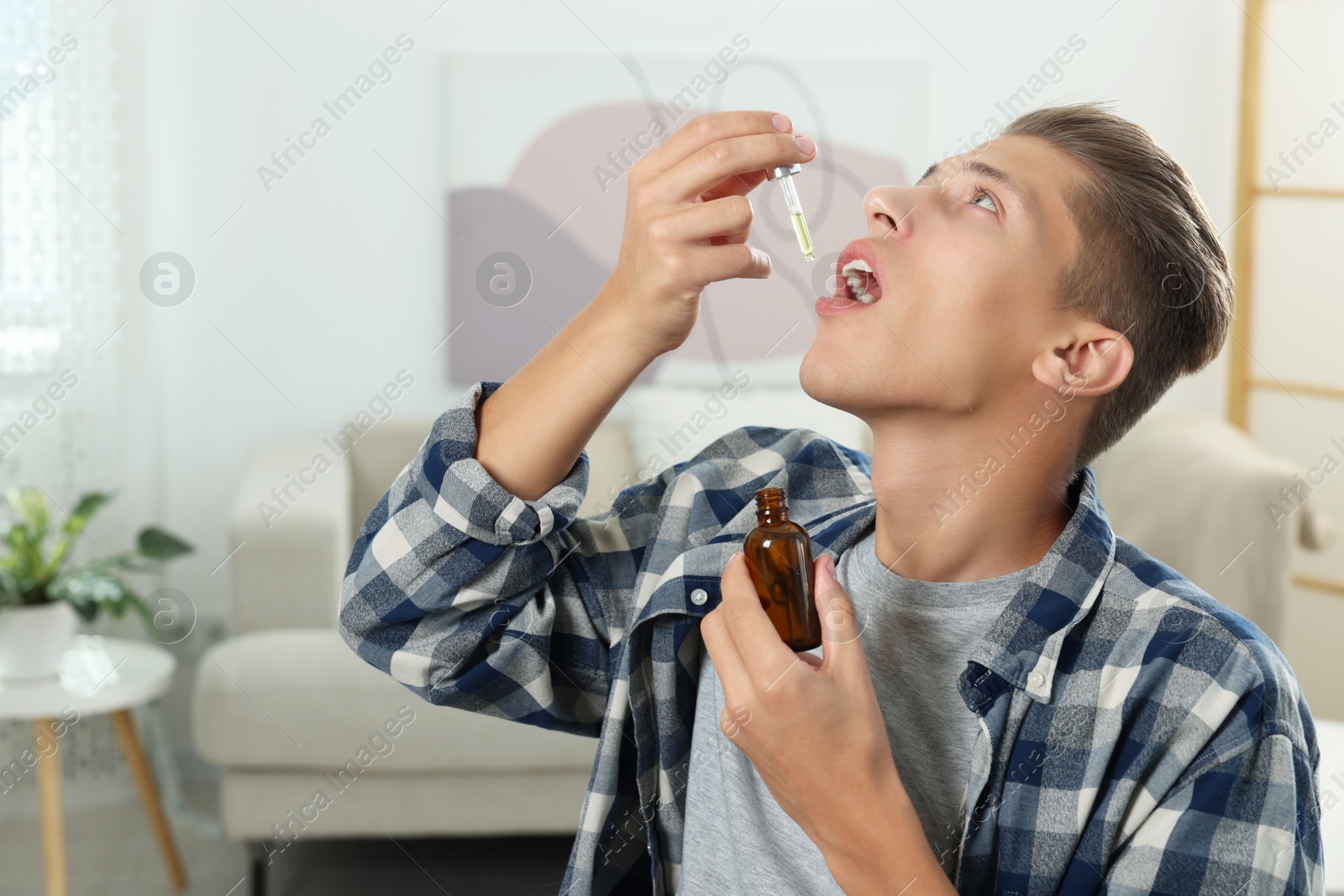 Photo of Young man taking CBD tincture indoors. Herbal extract