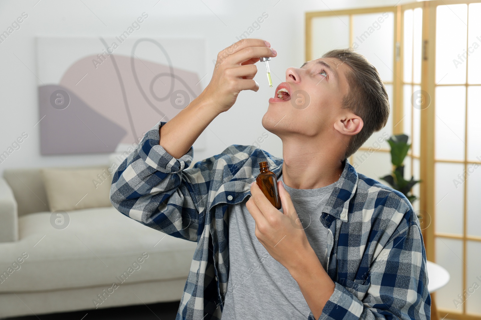 Photo of Young man taking CBD tincture indoors. Herbal extract