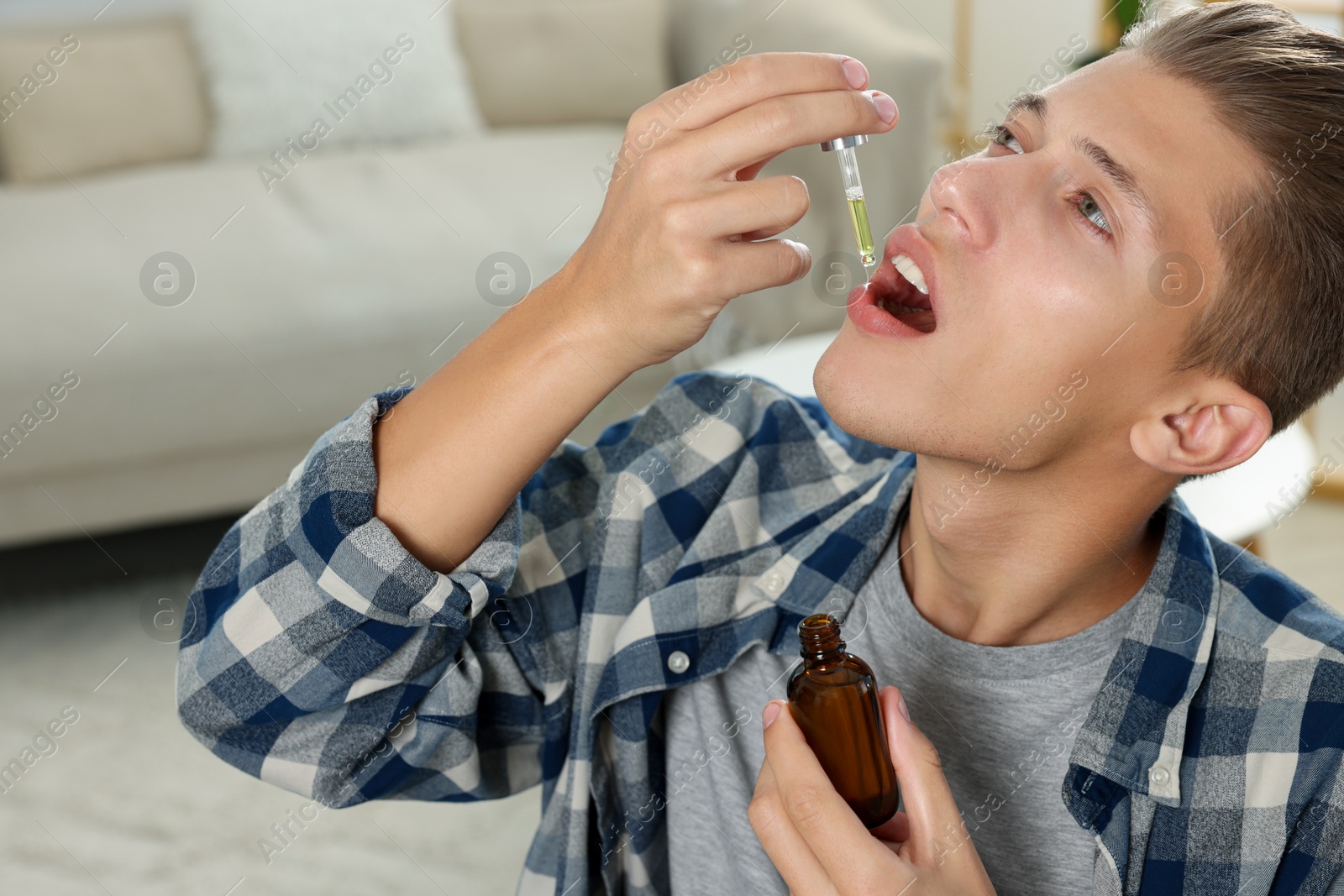 Photo of Young man taking CBD tincture indoors. Herbal extract