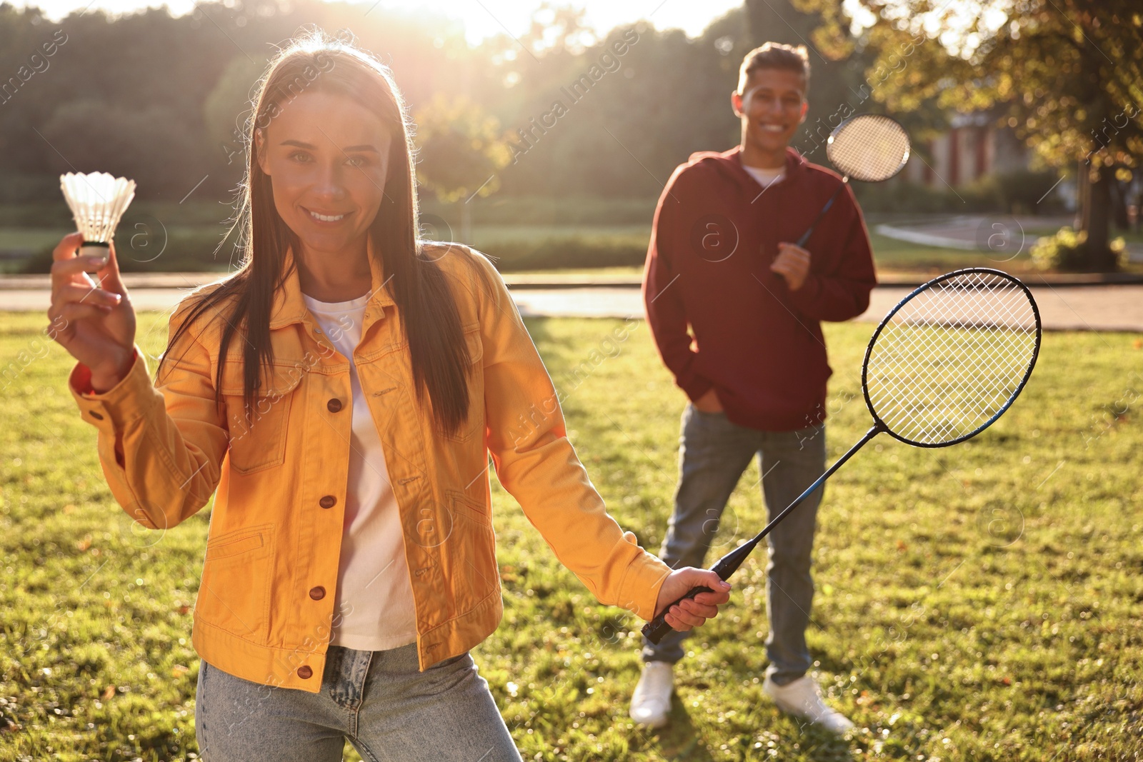 Photo of Young man and woman with badminton rackets and shuttlecock in park on sunny day, selective focus