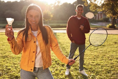 Photo of Young man and woman with badminton rackets and shuttlecock in park on sunny day, selective focus