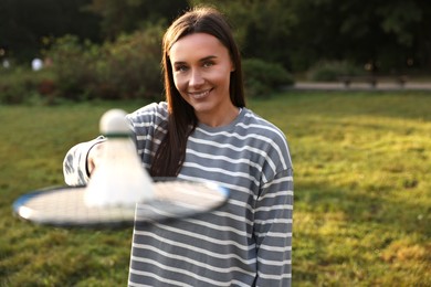 Photo of Happy young woman with badminton racket and shuttlecock in park, selective focus