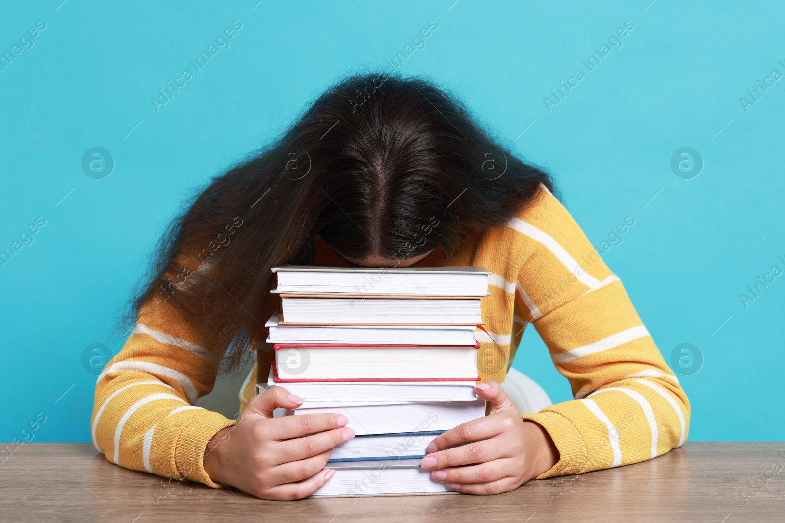 Photo of Young student with books having stress before exam at table against light blue background