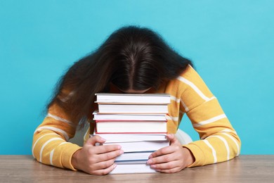 Young student with books having stress before exam at table against light blue background