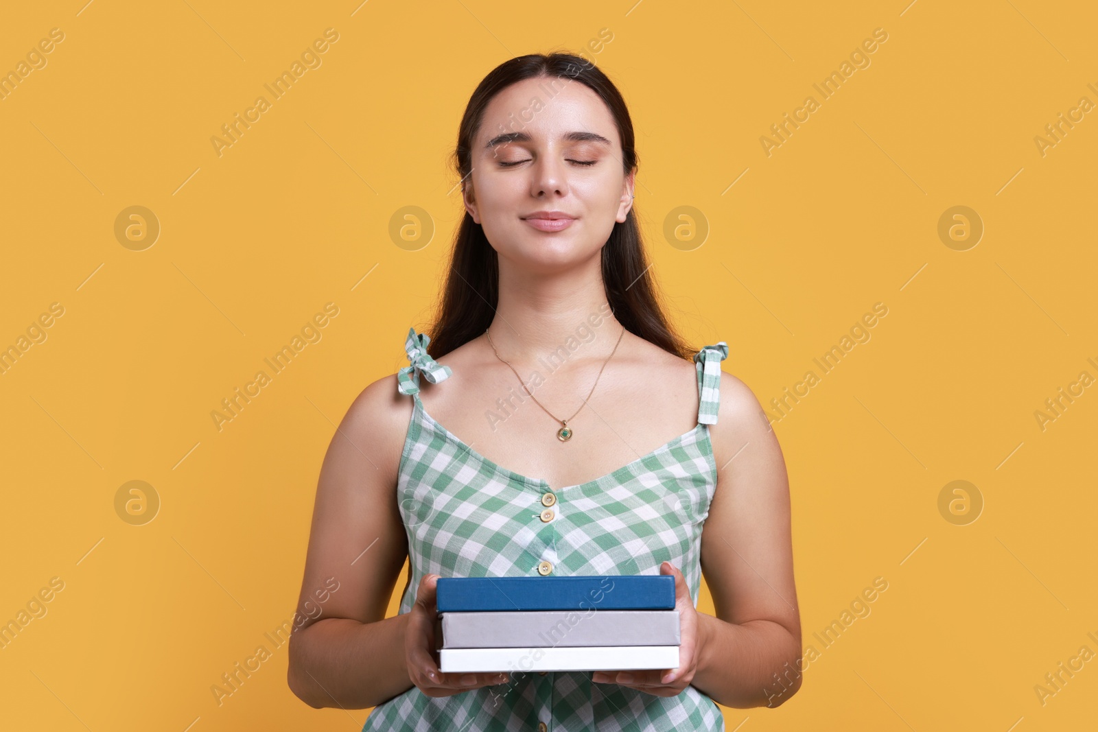 Photo of Young student with stack of books on orange background