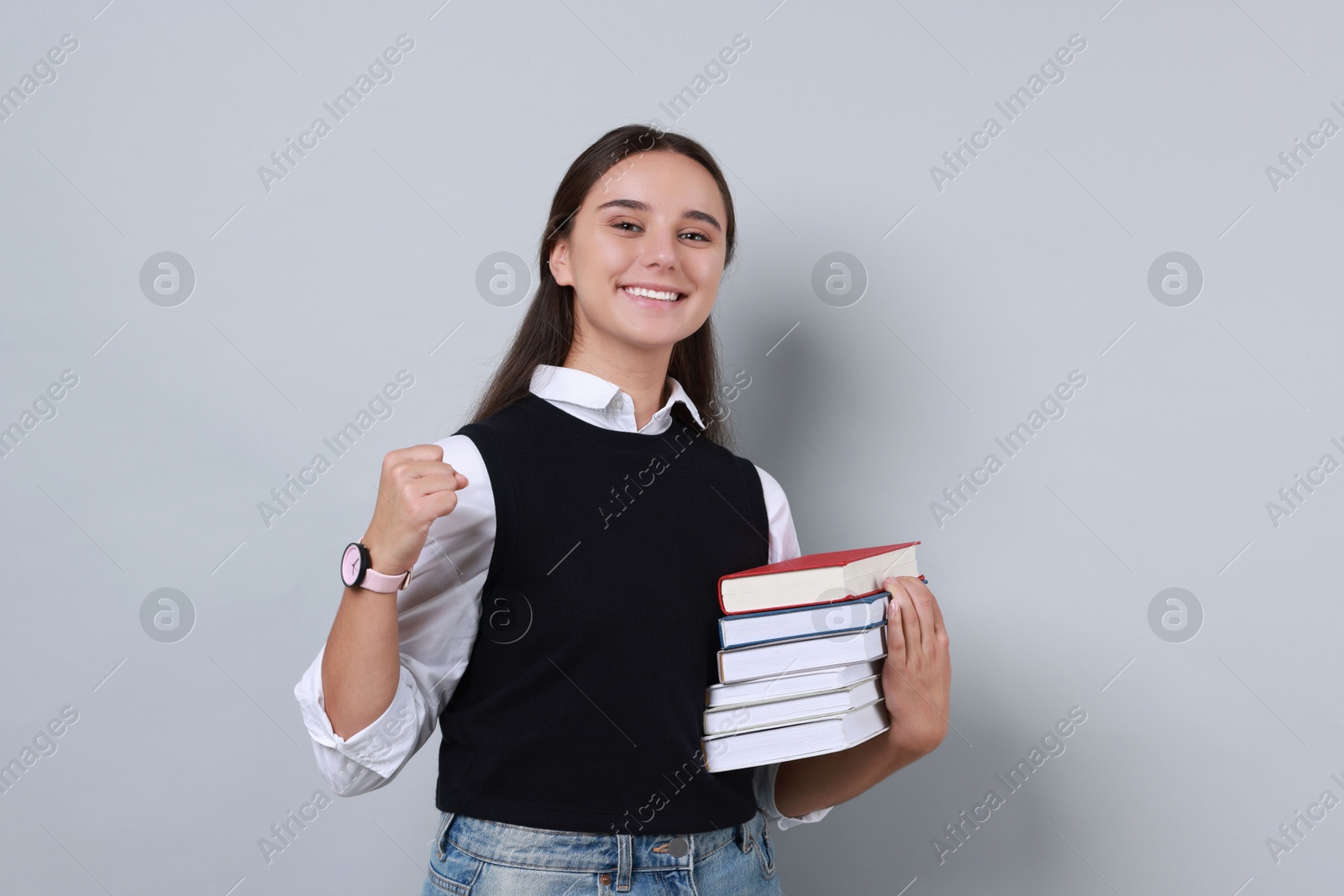 Photo of Young student with stack of books happy about her good exam result on grey background