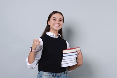 Photo of Young student with stack of books happy about her good exam result on grey background