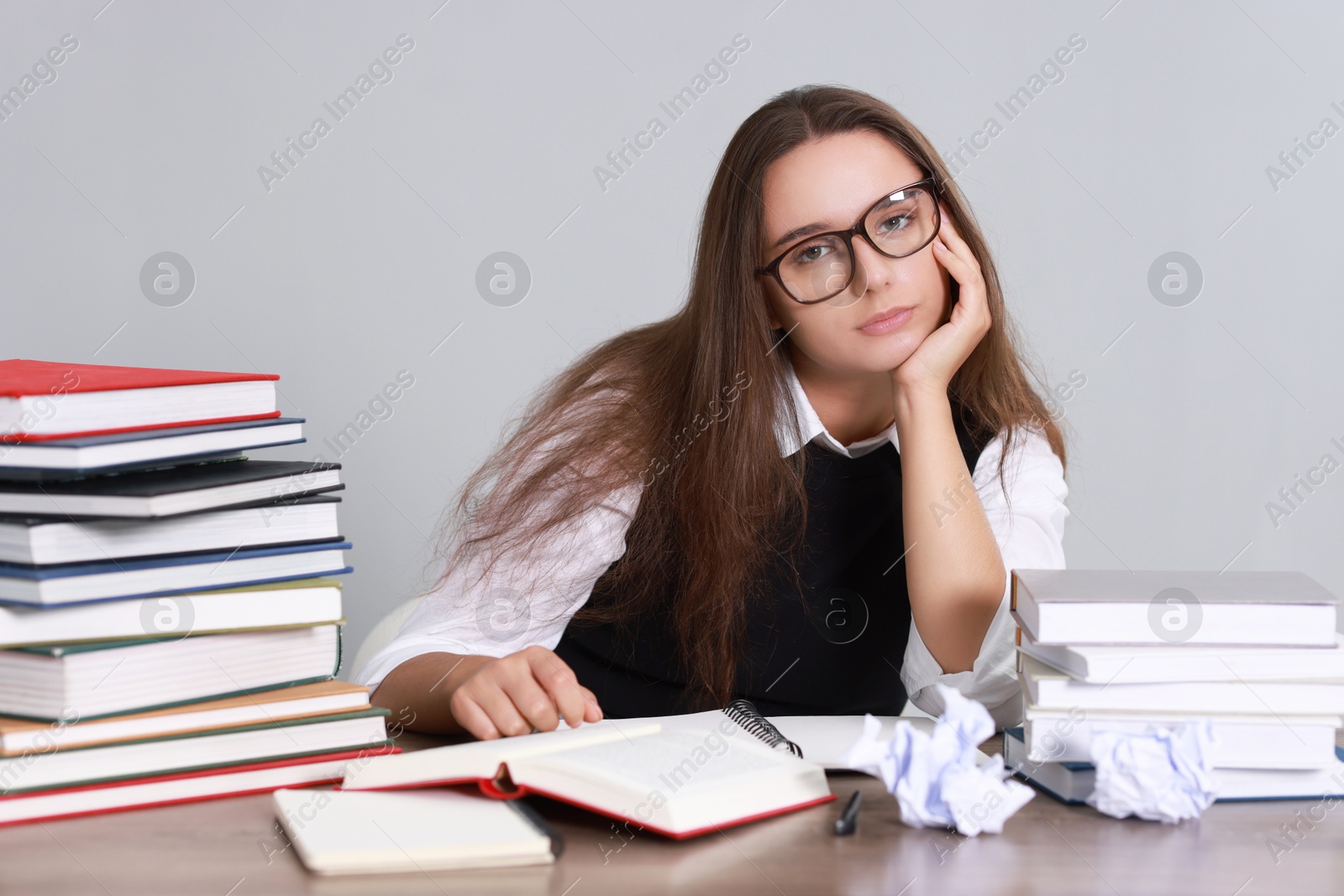 Photo of Young student having stress before exam at desk against grey background