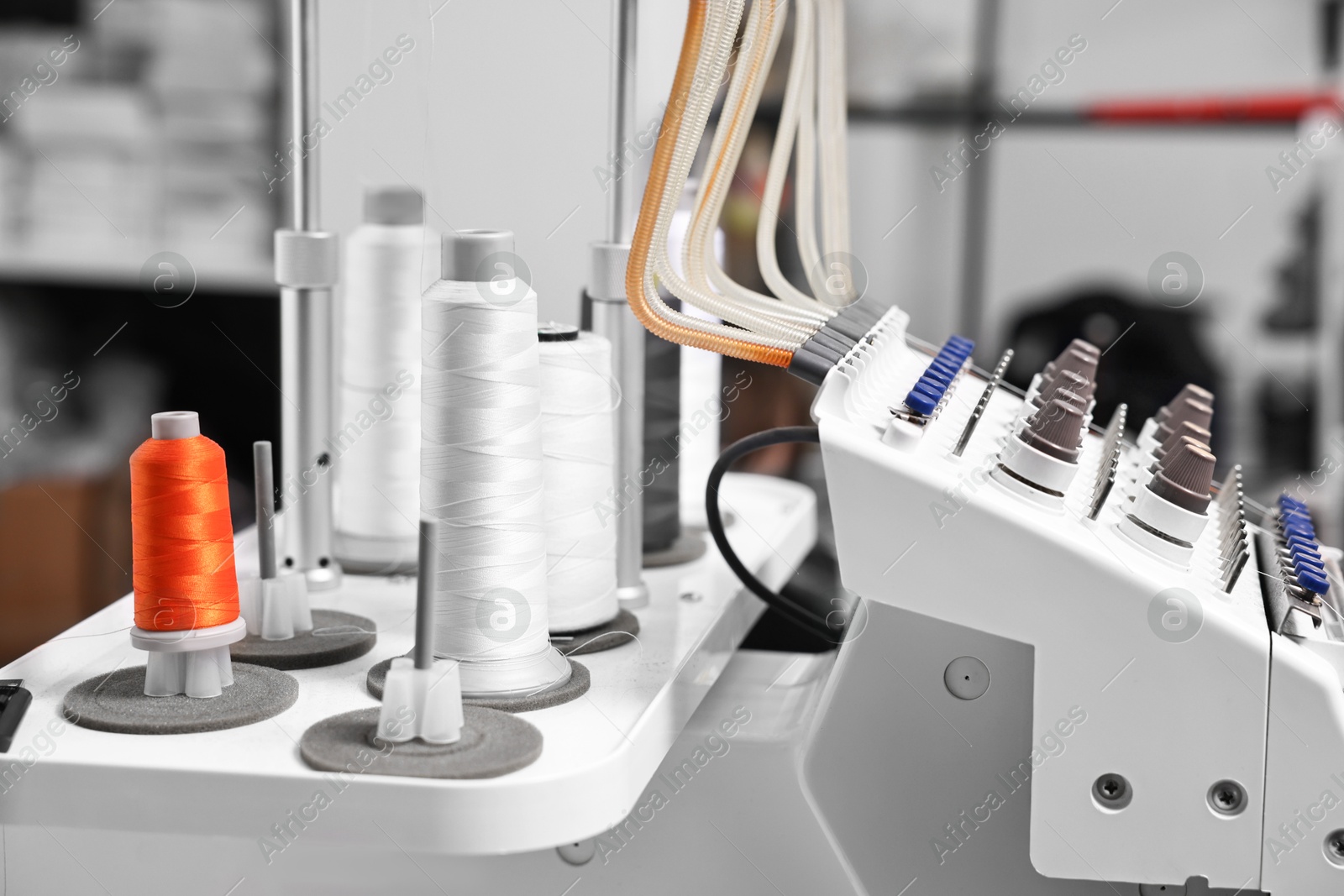 Photo of Sewing machine with spools of thread in professional workshop, closeup