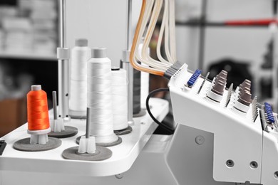 Photo of Sewing machine with spools of thread in professional workshop, closeup