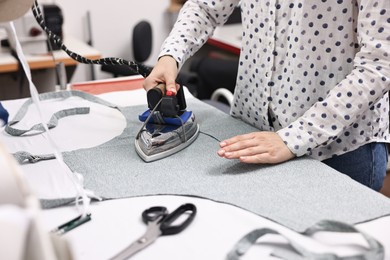 Photo of Young woman with iron working at white table in professional workshop, closeup