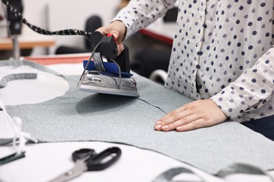 Photo of Young woman with iron working at white table in professional workshop, closeup