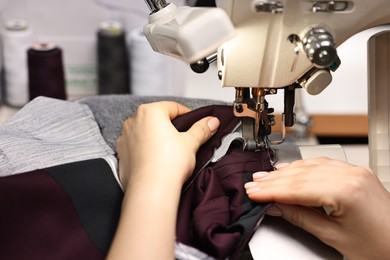 Photo of Young woman with sewing machine working in professional workshop, closeup