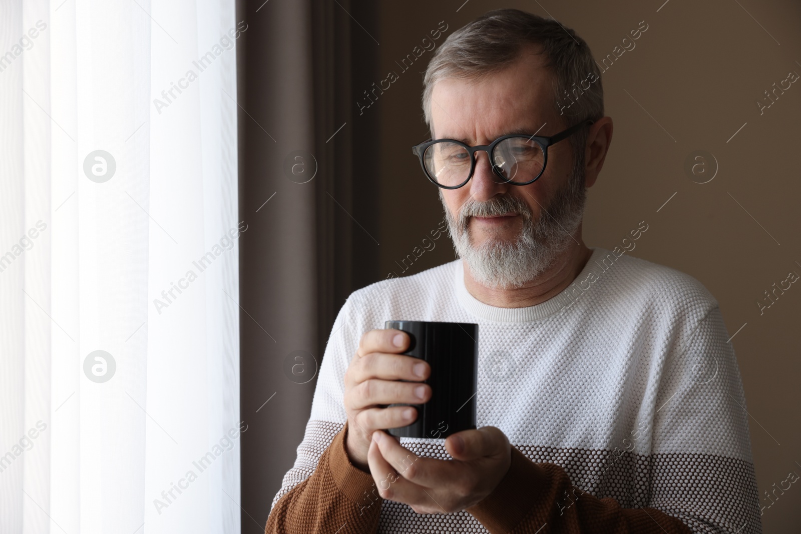 Photo of Mature man with cup of hot drink at home. Space for text