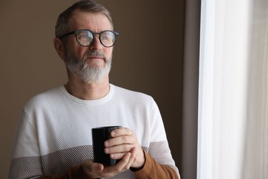 Photo of Mature man with cup of hot drink at home. Space for text