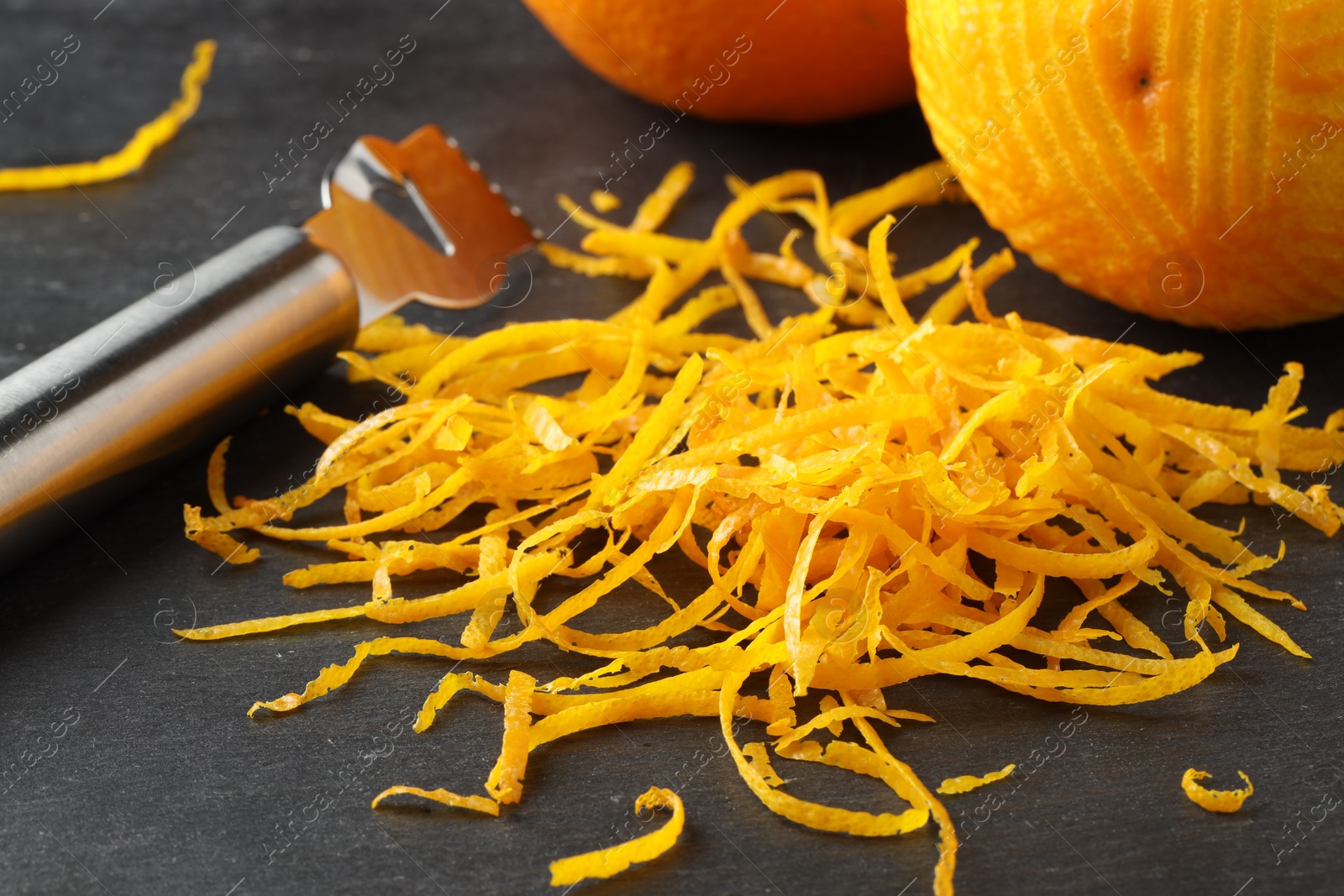 Photo of Fresh orange zest, zester and fruits on black table, closeup