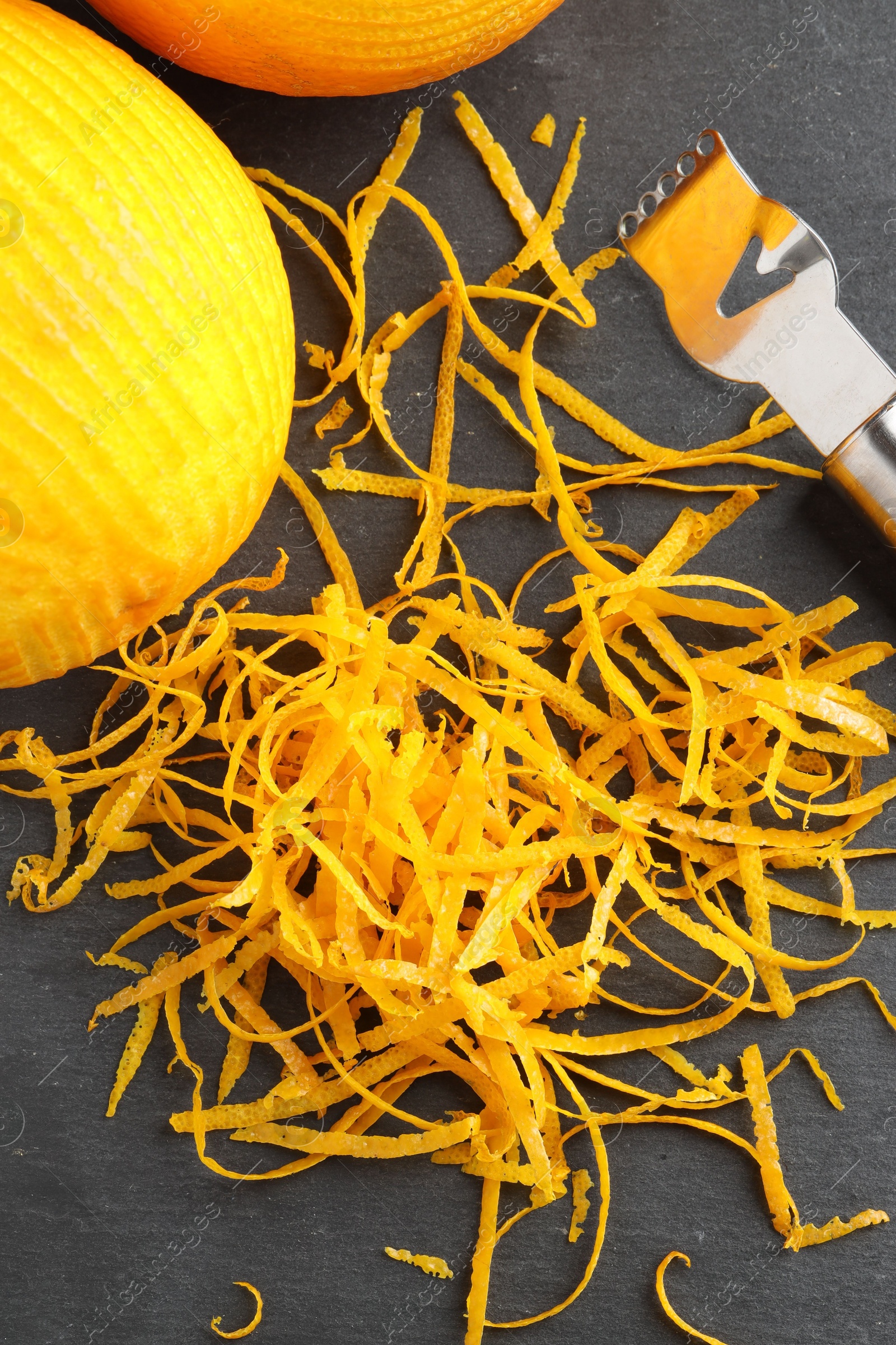 Photo of Fresh orange zest, zester and fruit on black table, flat lay