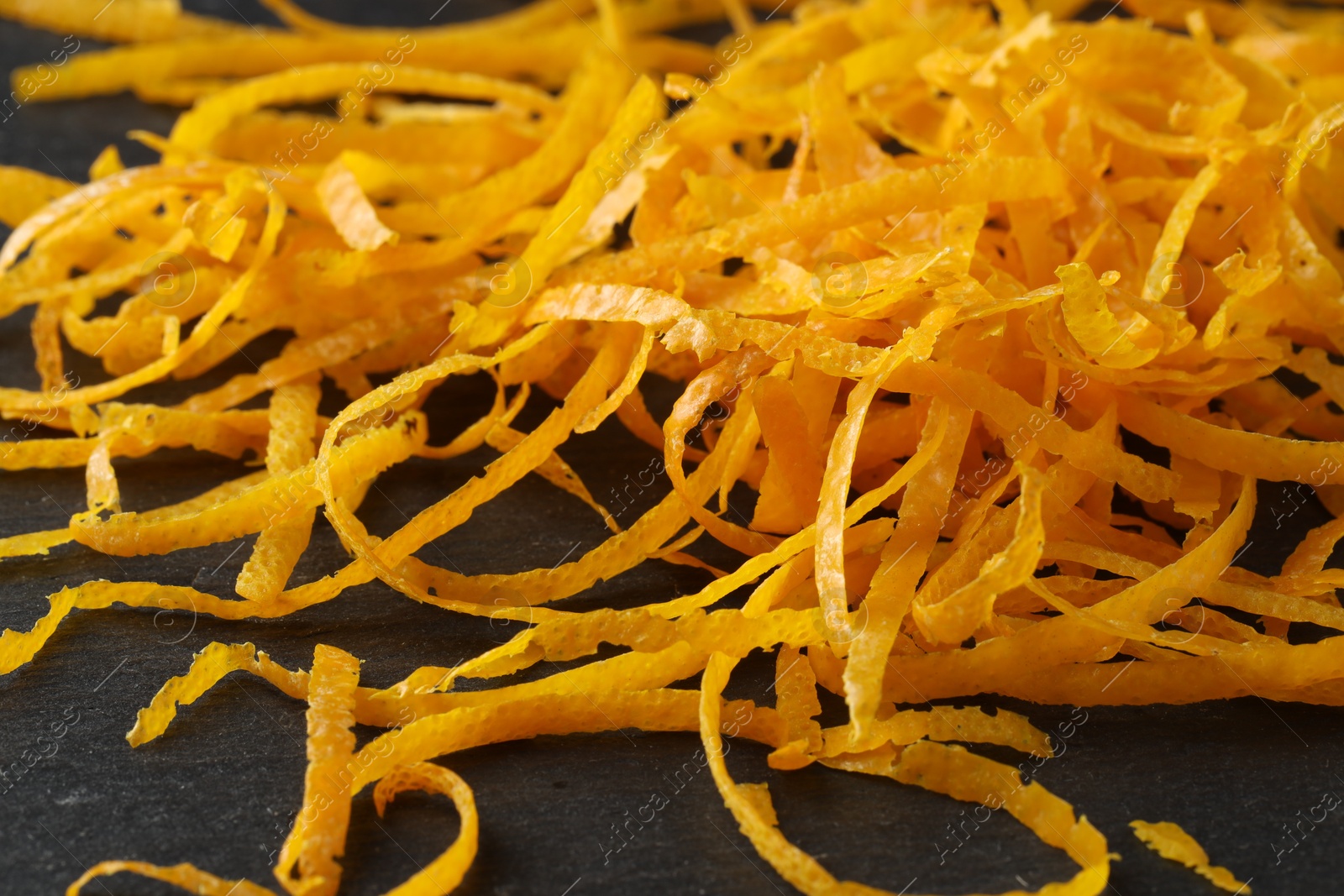 Photo of Pile of fresh orange zest on black table, closeup