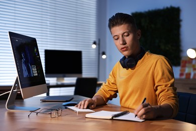 Designer taking notes while working on computer indoors at night